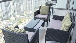 A balcony with wicker furniture, a glass table, and a view of high-rise buildings. - Modern 2BR Apartment Perfect for 4 in Business Bay (Dubai)