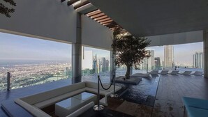 A high-rise building with a rooftop pool area featuring a glass-enclosed hot tub, lounge chairs, and a large tree. - Modern 2BR Apartment Perfect for 4 in Business Bay (Dubai)
