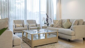Un salon moderne avec un ensemble de canapés, une table basse en verre et des rideaux légers.