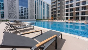 A modern hotel with a swimming pool, lounge chairs, and a large building with reflective windows. - Charismatic Studio in Laya Heights Perfect for 2 (Dubai)