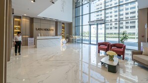 A modern hotel lobby with a marble floor, a reception desk, and large windows offering a view of the city. - Heart Captivating Studio in Laya Heights (Dubai)