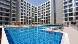 A modern building with a central swimming pool, surrounded by balconies and a covered area with seating. - Heart Captivating Studio in Laya Heights (Dubai)