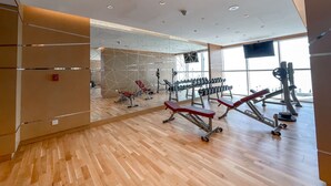 A modern gym with wooden flooring, exercise equipment, and large windows. - Majestic Studio in Damac Carson C (Dubai)