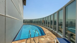 A rooftop swimming pool with clear blue water, surrounded by glass walls offering city views. - Stylish Studio Apartment in Tecom s Prime Location (Dubai)