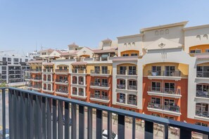 Filare di edifici residenziali a più piani, con balconi, cielo sereno e strada in primo piano.
