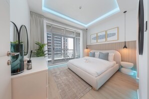 Ein modernes Schlafzimmer mit einem großen Bett, einem Glastisch, Blick auf die Stadt und einem Balkon mit Geländer.