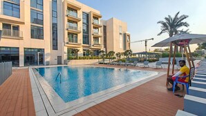 A swimming pool with lounge chairs, a covered seating area, and a modern building with balconies. - Elegant Relaxing 3-bedroom Apartment in Perfect Location at Canal Front 6 (Dubai)