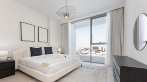 A modern bedroom with a large bed, a nightstand, a dresser, a large window with curtains, and a city view. - Elegant Relaxing 3-bedroom Apartment in Perfect Location at Canal Front 6 (Dubai)