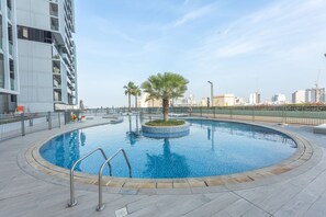 A swimming pool with a palm tree in the center, surrounded by a fence, with a cityscape in the background. - Majestic Studio in Bloom Tower C Perfect for 2 (Dubai)