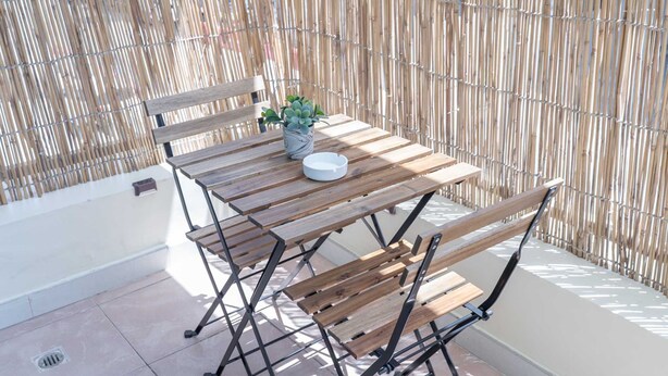 Ein Holztisch mit einem Blumentopf und einer weißen Schüssel, vor einer Bambus-Umzäunung.