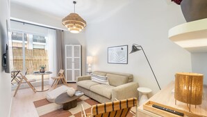 Ein modernes Wohnzimmer mit Sofa, Sessel und Couchtisch, ein Essbereich mit Tisch und Stühlen sowie ein großes Fenster mit Blick auf ein Gebäude.