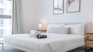 A neatly made bed with towels and a shoe, a bedside lamp, and two framed pictures on the wall. - 1606 DEC Tower 1 in Dubai (Dubai)