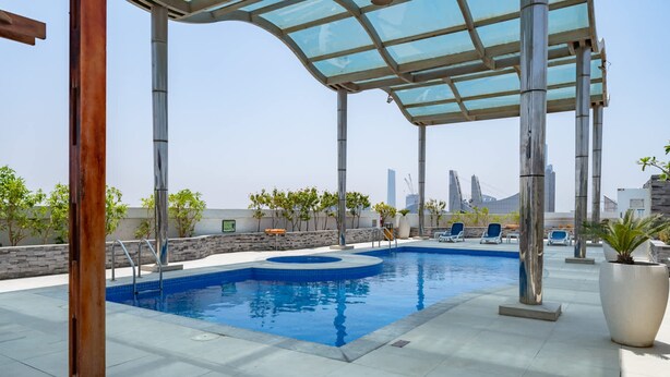 A rooftop pool with a glass canopy, lounge chairs, and a city skyline in the background. - Spacious Serene 2 Bedroom in JLT for 4 (Dubai)
