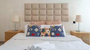 Un lit bien fait, avec une tête de lit capitonnée, deux tables de chevet avec des lampes et des coussins décoratifs.