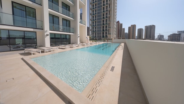 Una piscina en la azotea con sillas de descanso, rodeada de edificios altos.