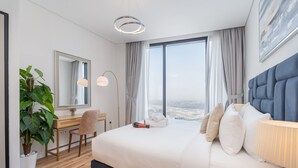 Ein modernes Hotelzimmer mit einem großen Bett, einem Schreibtisch, einem Sessel, einer Zimmerpflanze und Blick auf die Stadt.