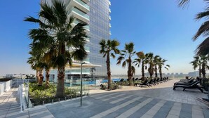 A modern building with a glass facade, palm trees, and a tiled patio with lounge chairs. - 2423 Carson B in Dubai (Dubai)