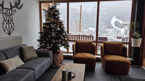 Ett modernt vardagsrum med ett stort fönster, en julgran, en soffa, två fåtöljer och ett soffbord.
