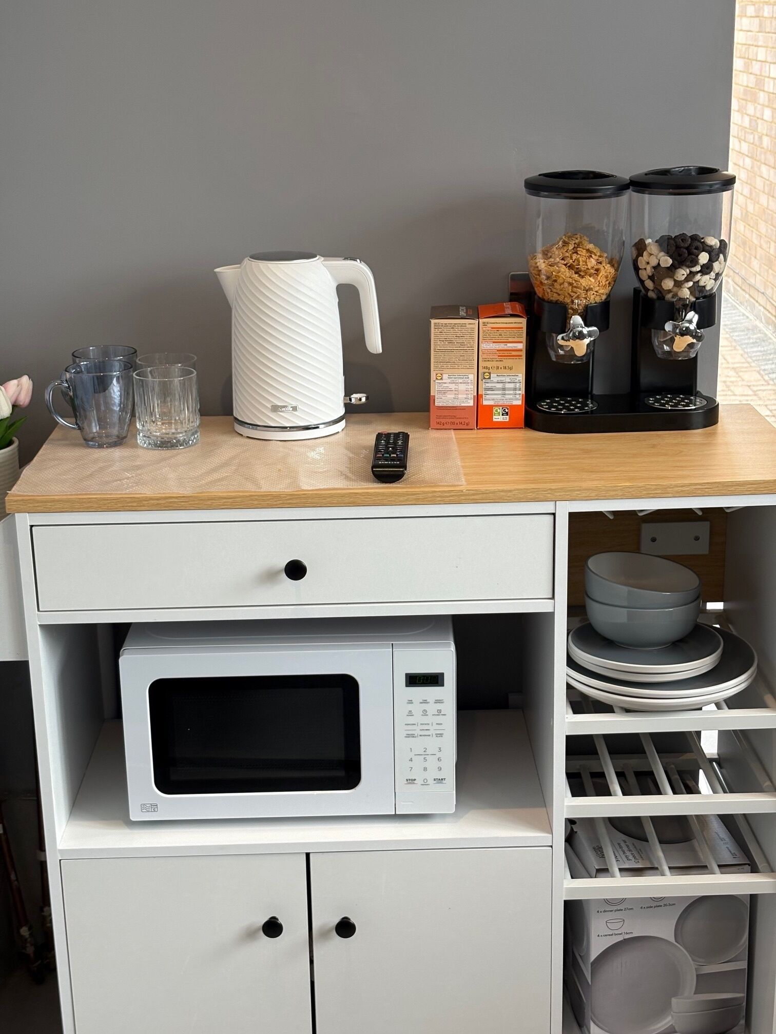 A kitchenette with a microwave, kettle, coffee machine, and storage for dishes.