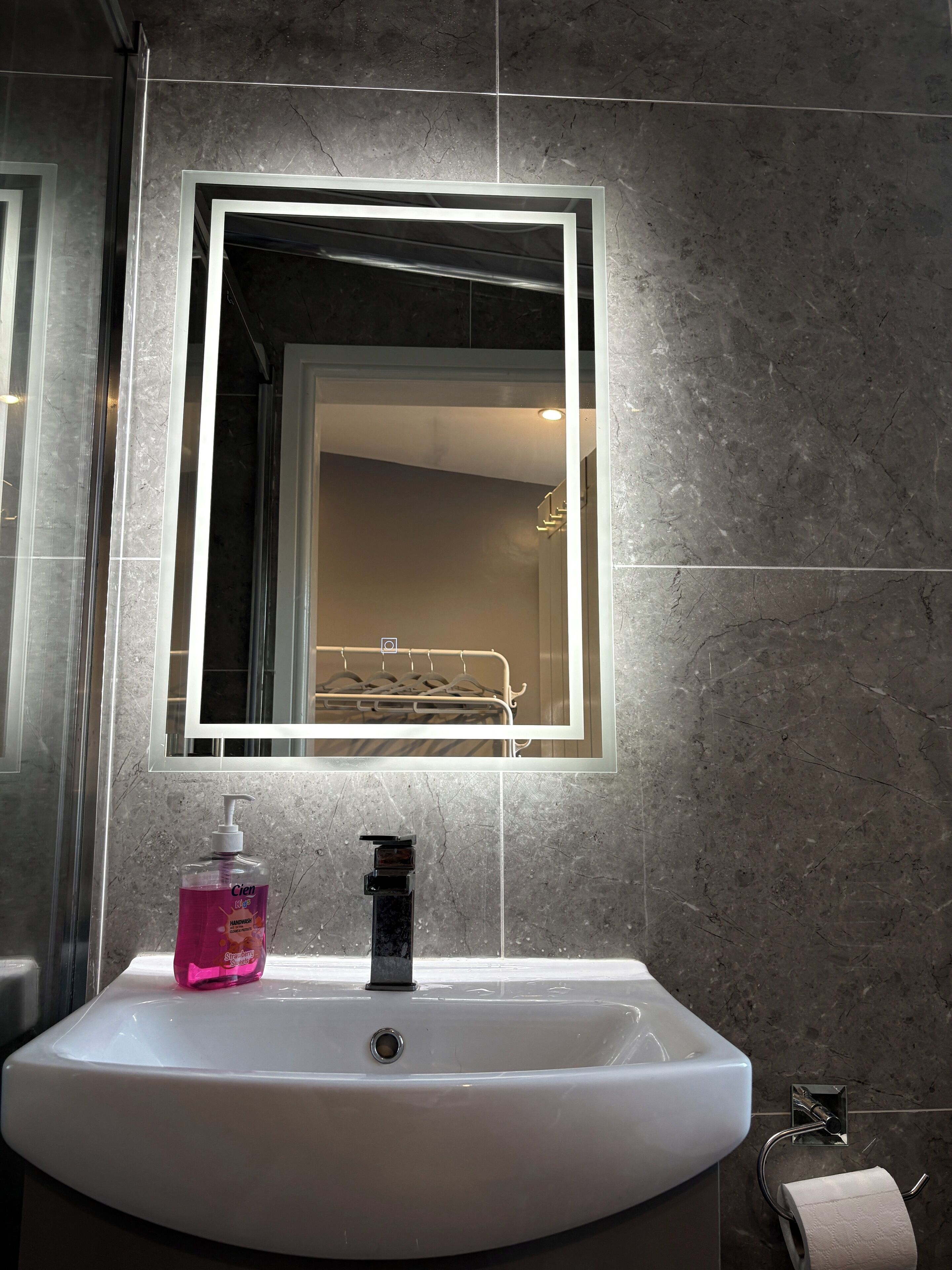 A bathroom with a white sink, a mirror with a light, and a hand soap dispenser.
