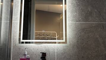 A bathroom with a white sink, a mirror with a light, and a hand soap dispenser.