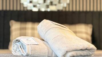 A neatly made bed with a folded towel and a tag, a textured gray pillow, and a wall with a geometric mirror design.