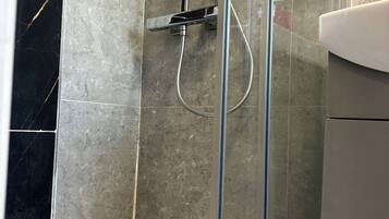 A bathroom with a glass-enclosed shower, a white bathtub, and a bottle of shampoo on the floor.