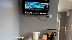 A kitchenette with a microwave, a coffee maker, and a small cabinet with dishes. - The Garden Studio (Luton)