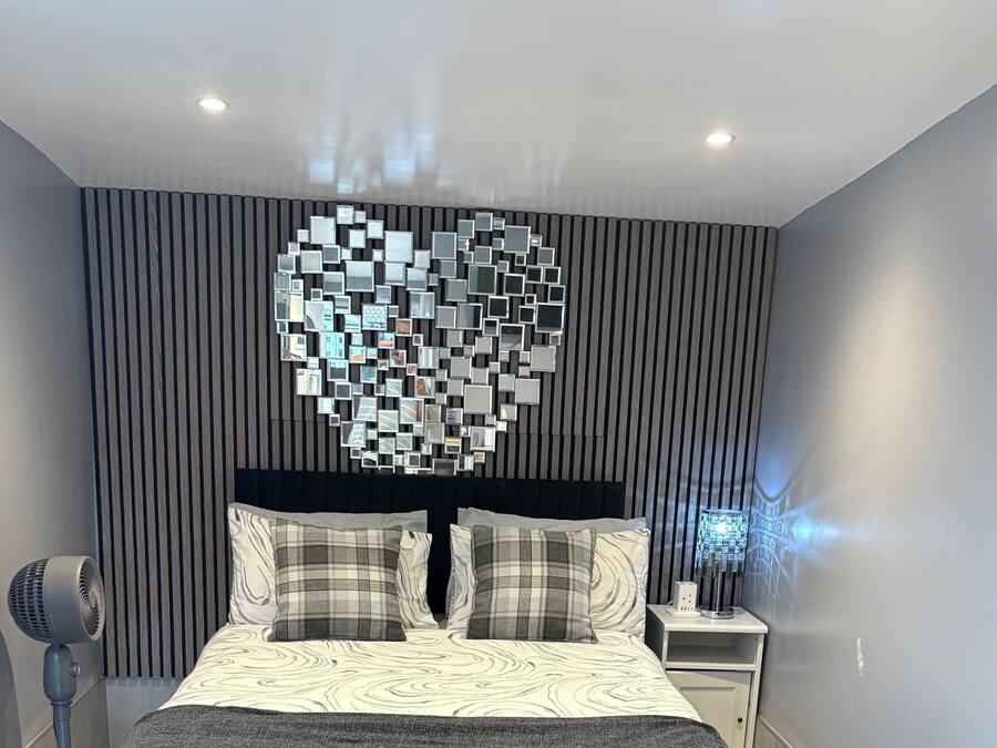Un dormitorio moderno con una cama, una lámpara con forma de corazón montada en la pared, una mesita de noche y una lámpara de pie.