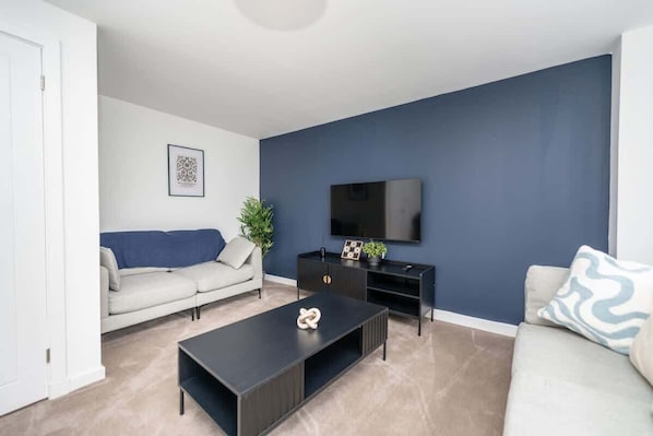 Ein Wohnzimmer mit einer Couch, einem Couchtisch, einem Fernseher und einer dunkelblauen Wand.