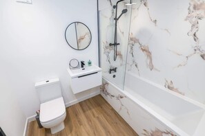 Ein Badezimmer mit Toilette, Waschbecken, Spiegel und einer Dusche mit Marmorwand.