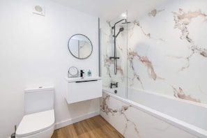 Un baño con inodoro, lavabo con espejo y ducha con cabina de vidrio.