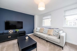 A modern living room with a flat-screen TV, a sofa, a coffee table, and a TV stand with decorative items. - The Gordon | Vacant Nests | Heart of Aberdeen (Aberdeen)