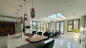 A spacious kitchen with a central island, modern pendant lighting, and large windows offering views of the outdoors. - Bluebell House (London)