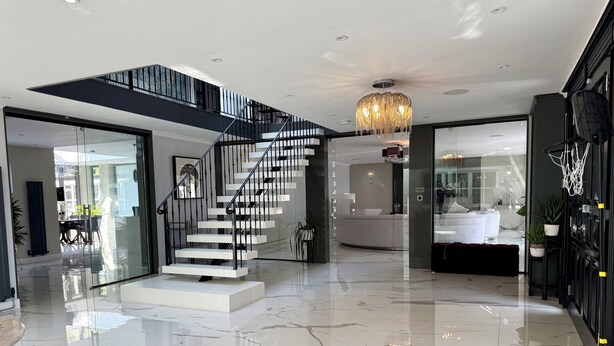 A modern interior with a central staircase, a chandelier, and a clean, polished floor. - Bluebell House (London)