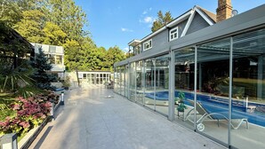 A modern house with a glass-enclosed patio, a swimming pool, and a garden with various plants. - Bluebell House (London)