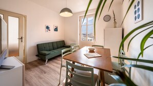 Een moderne woonruimte met een houten eettafel, een groene bank en witte stoelen. In het midden staat een klein rond tafeltje met een schaal.