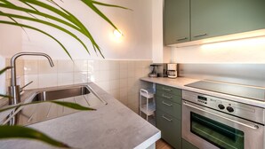 Een moderne keuken met een RVS spoelbak, een inbouwoven en groene kastjes.