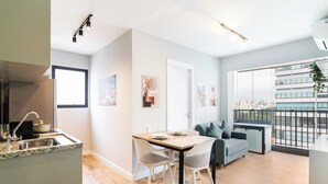 A modern apartment with a kitchen, dining area, and living room. It features a large window with a city view, a balcony, and a flat-screen TV. - Bourbon Smart Style (São Paulo)