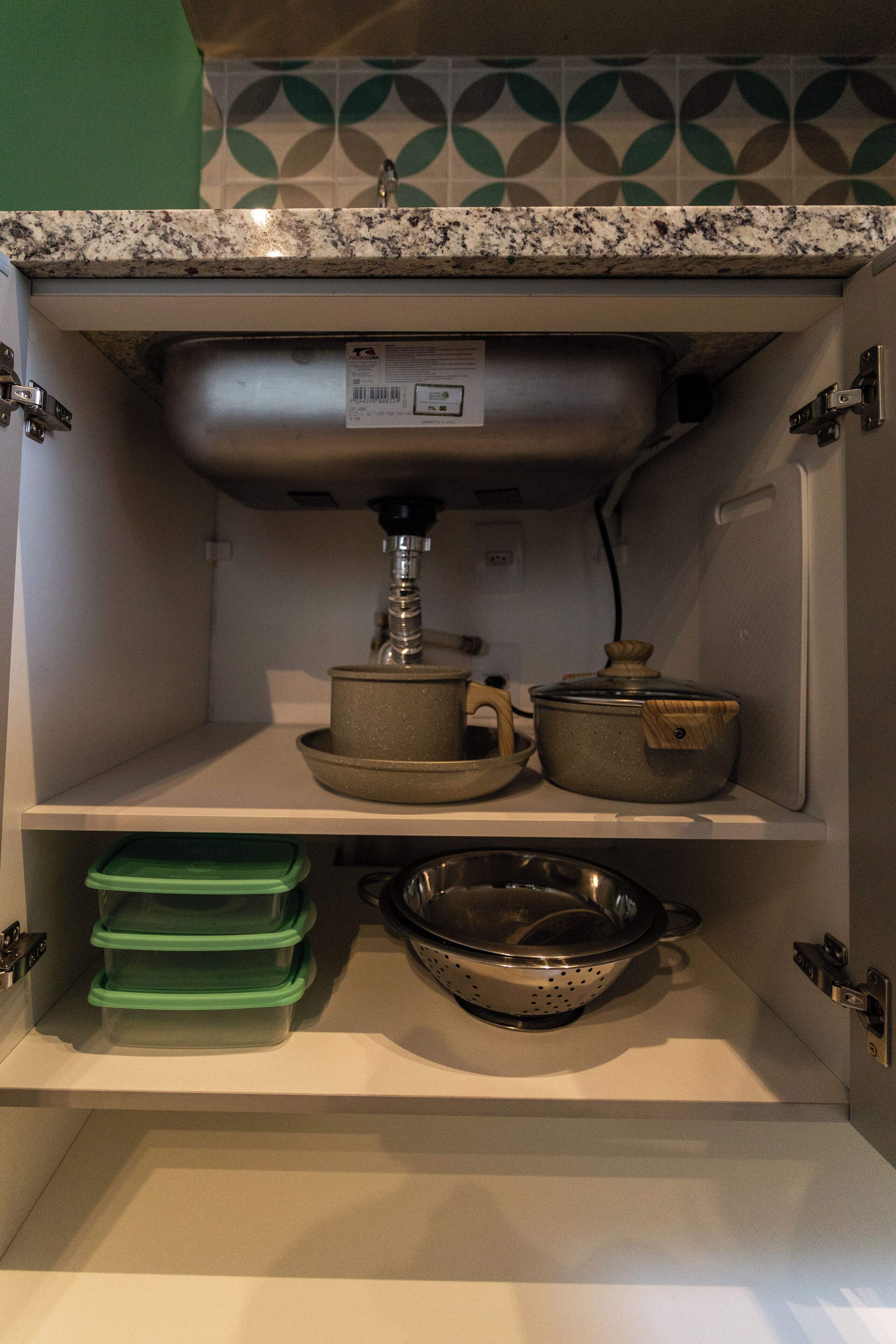 A kitchen with a stainless steel sink, a colander, and two pots on the counter.