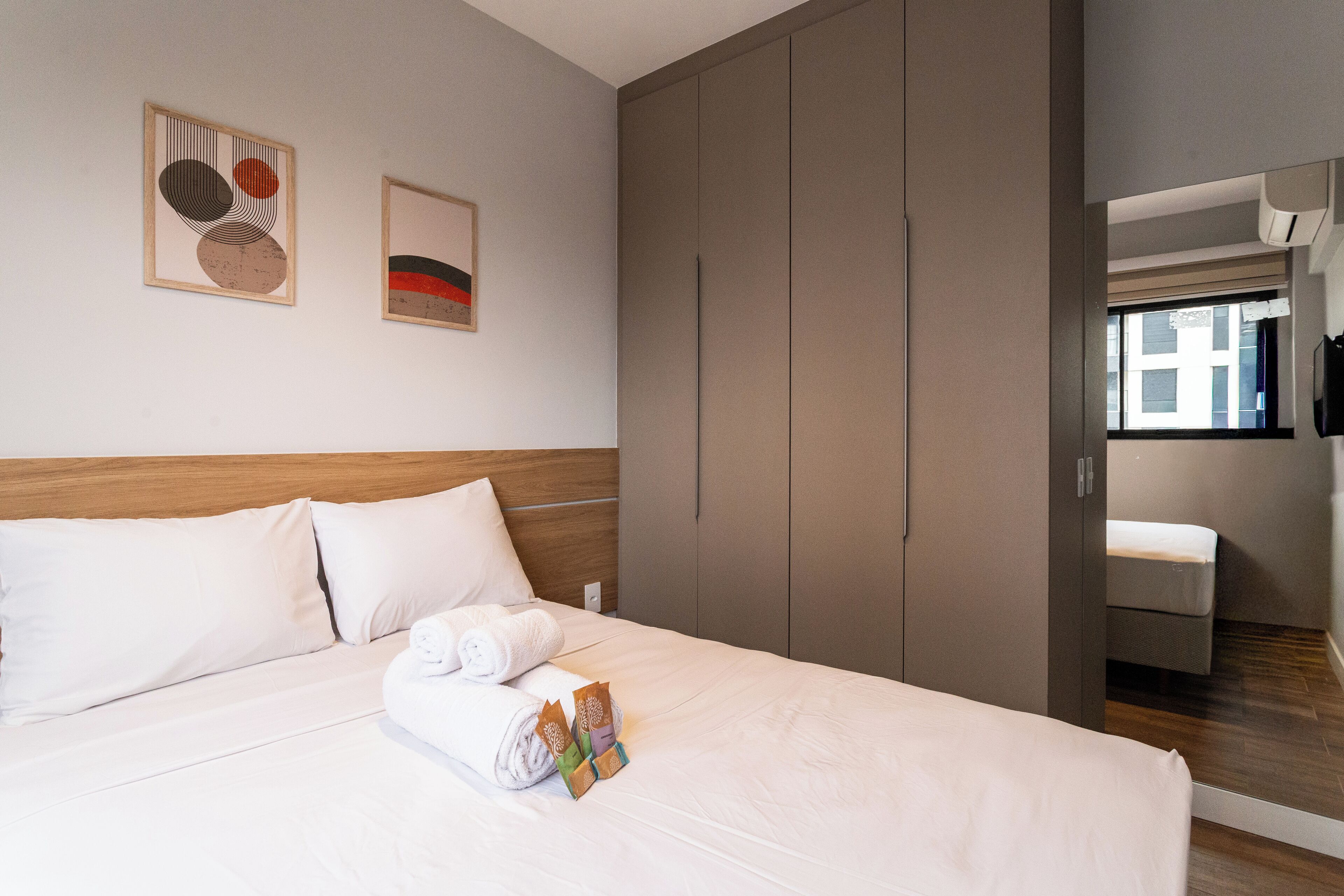 A neatly made bed with white linens, a wooden headboard, and a set of towels and toiletries on the bed.