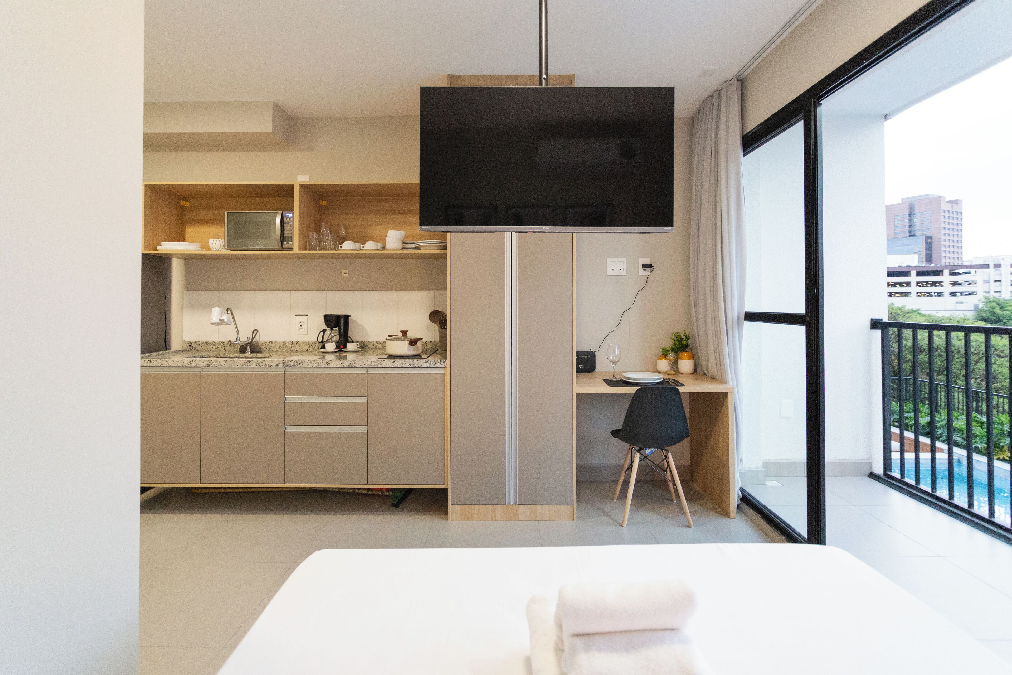 Una cucina moderna con una TV a schermo piatto, un'area pranzo con tavolo e sedie, e un balcone con vista sulla piscina.