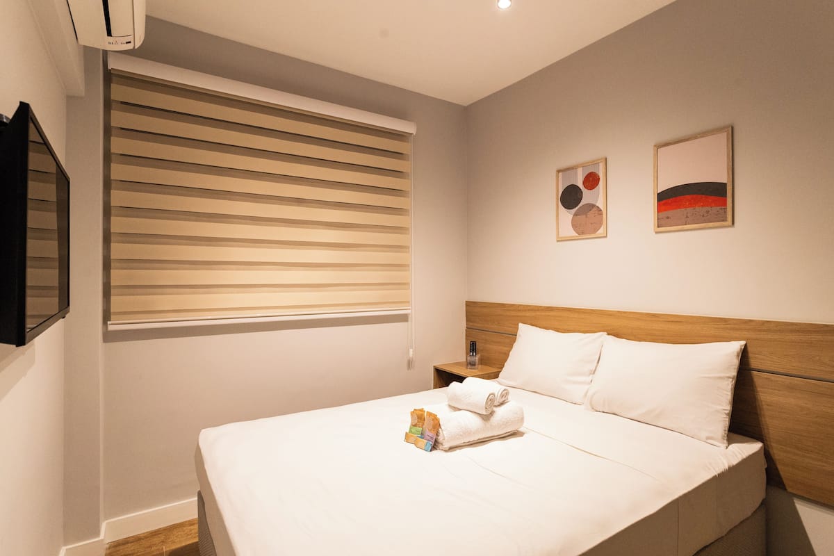 A neatly made bed with white linens, a wooden headboard, and a small bedside table with a lamp.