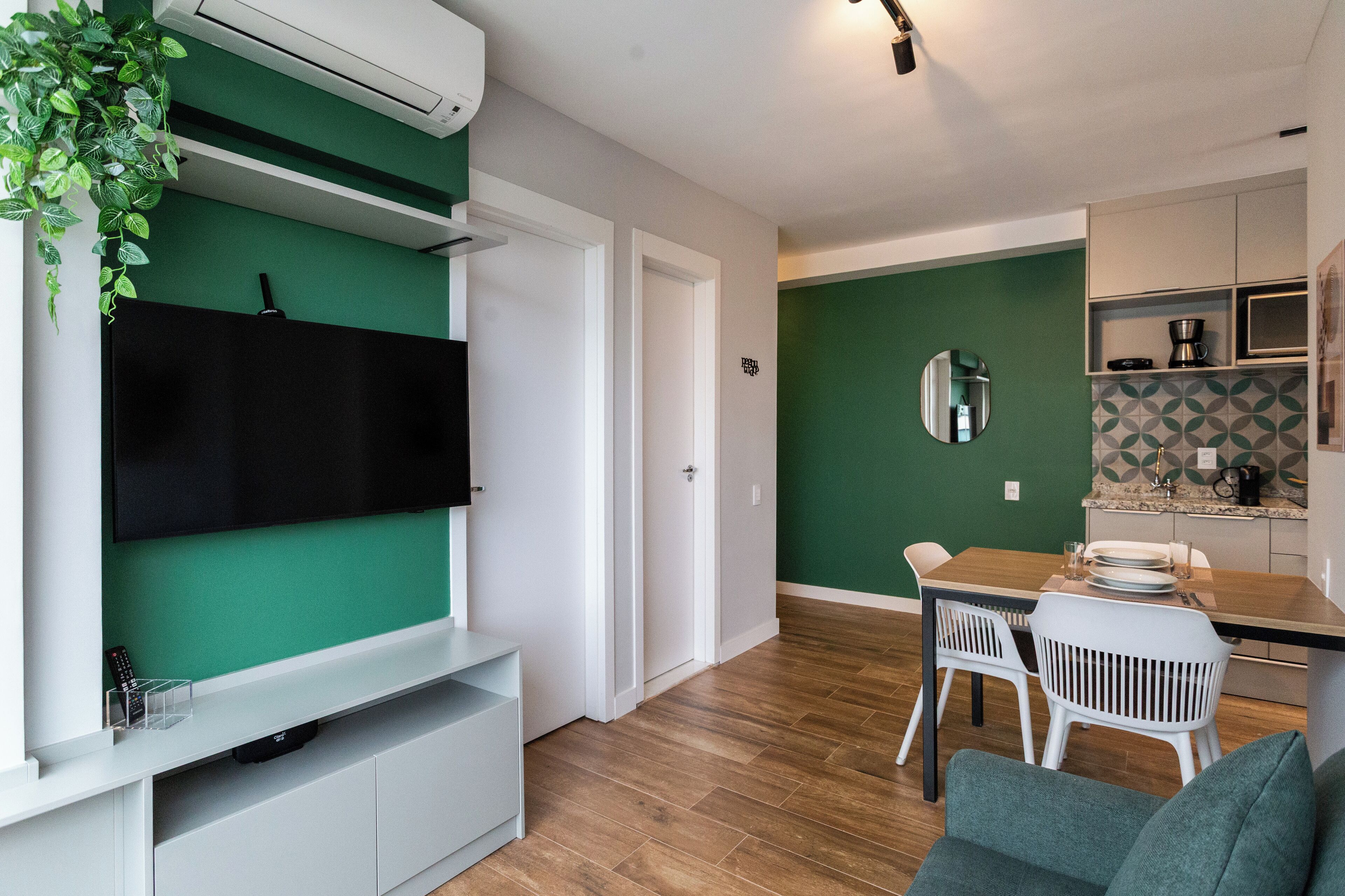 Un salon moderne doté d’un téléviseur à écran plat, d’un mur vert et d’un coin repas avec une table et des chaises.