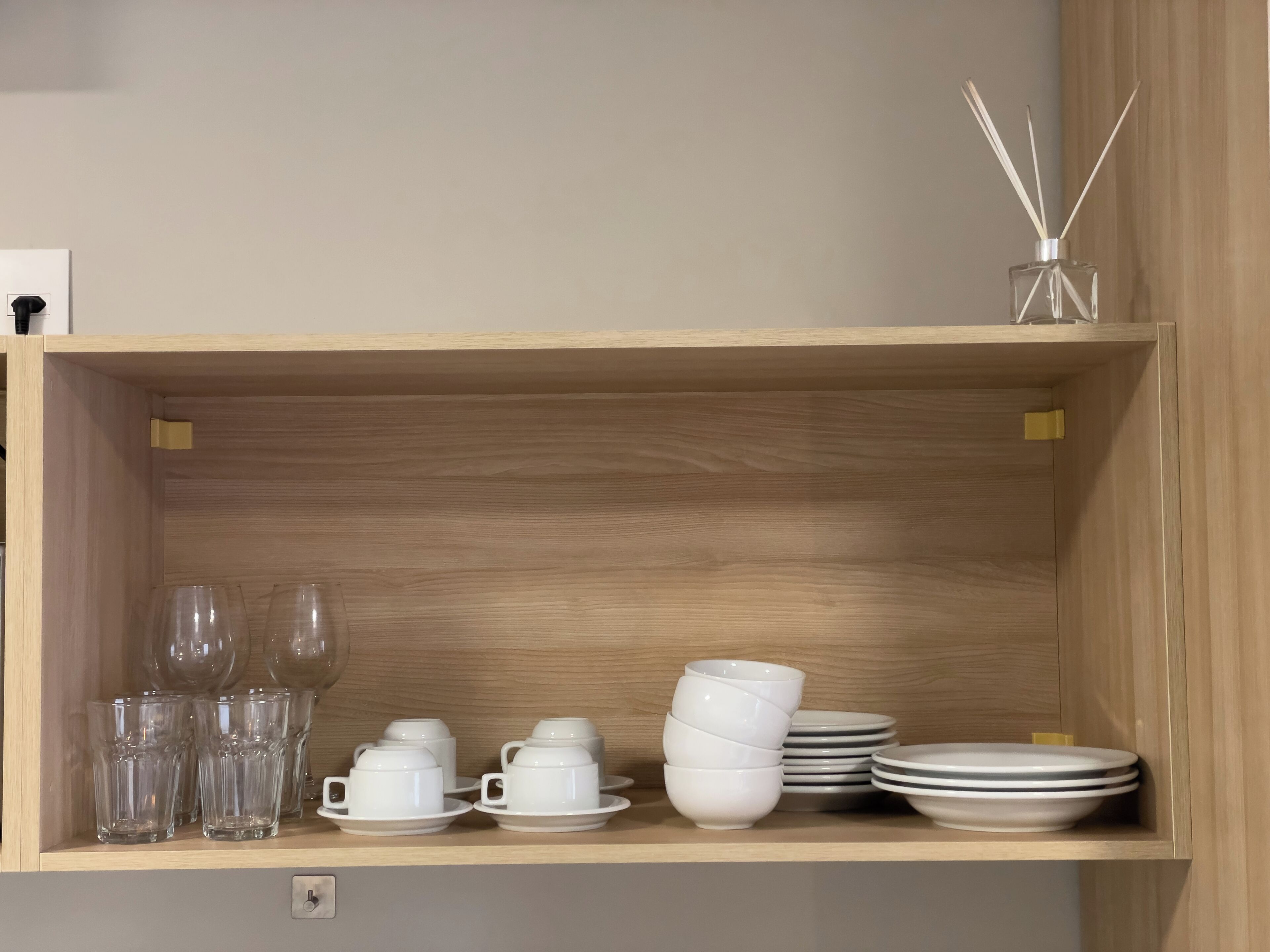 A wooden shelf with clear glassware, white cups, saucers, and plates.