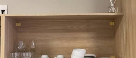 A wooden shelf with clear glassware, white cups, saucers, and plates.