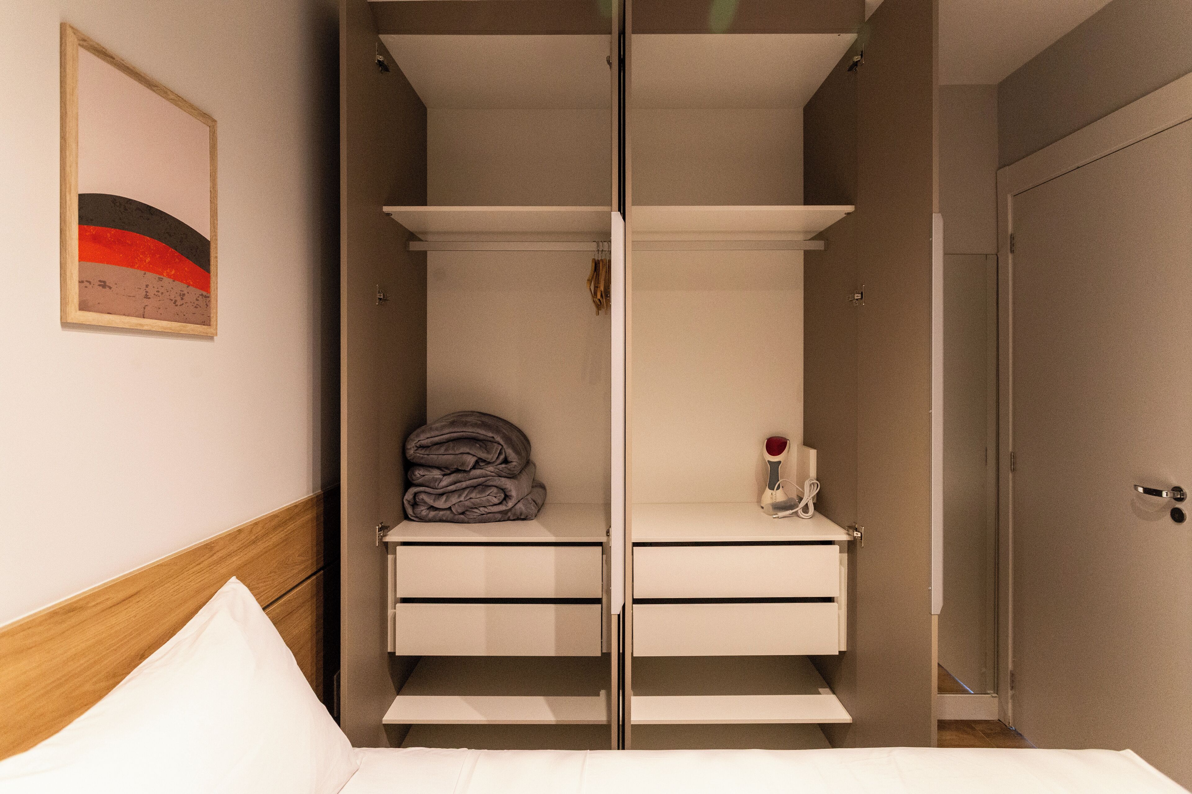 A hotel room with a bed, a wardrobe with a mirror, and a framed picture on the wall.