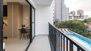 A balcony with a pool, a dining area with a chair, and a view of tall buildings. - Bourbon Smart Style (São Paulo)