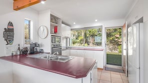 A modern kitchen with a large island, built-in appliances, and a view of the garden. - We’re thrilled to introduce this stunning new listing with The Lifestyle Group, Crescent Head. (Crescent Head)