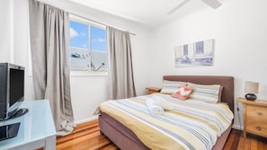 A hotel room with a bed, a TV, a window with curtains, a painting on the wall, and a lamp on the nightstand. - We’re thrilled to introduce this stunning new listing with The Lifestyle Group, Crescent Head. (Crescent Head)